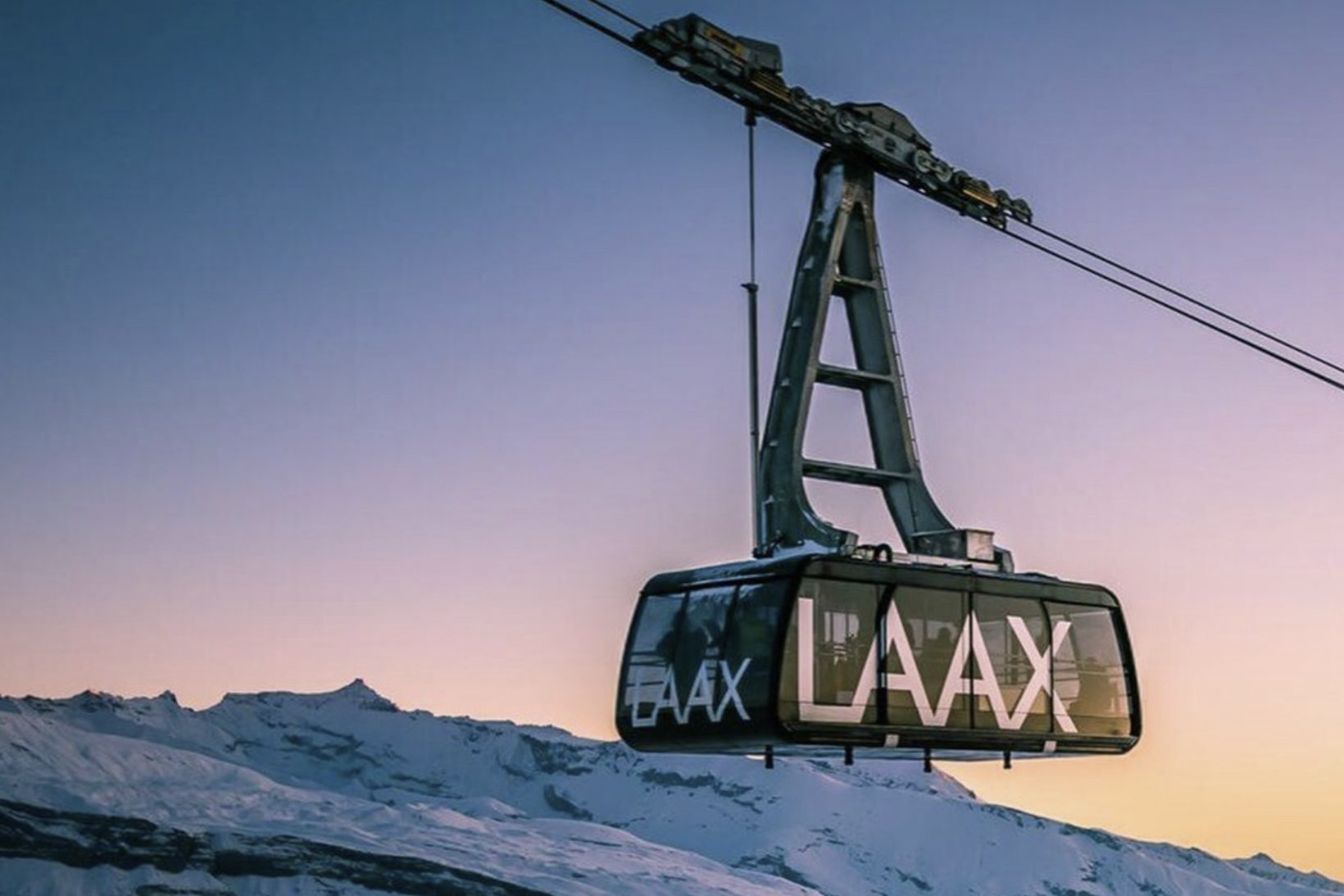 The LAAX aerial cable car crossing above a snow-covered ridge at sunset